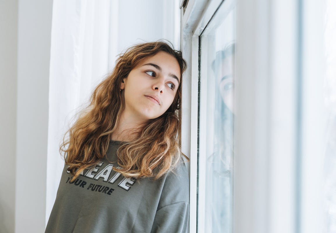 Unhappy Teenager Girl Looking Through Windowsill